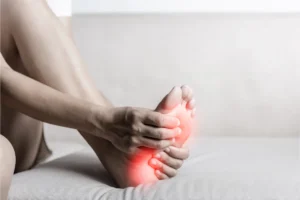 Mulher sentada no sofá sentindo dor no pé devido a fascite plantar.
