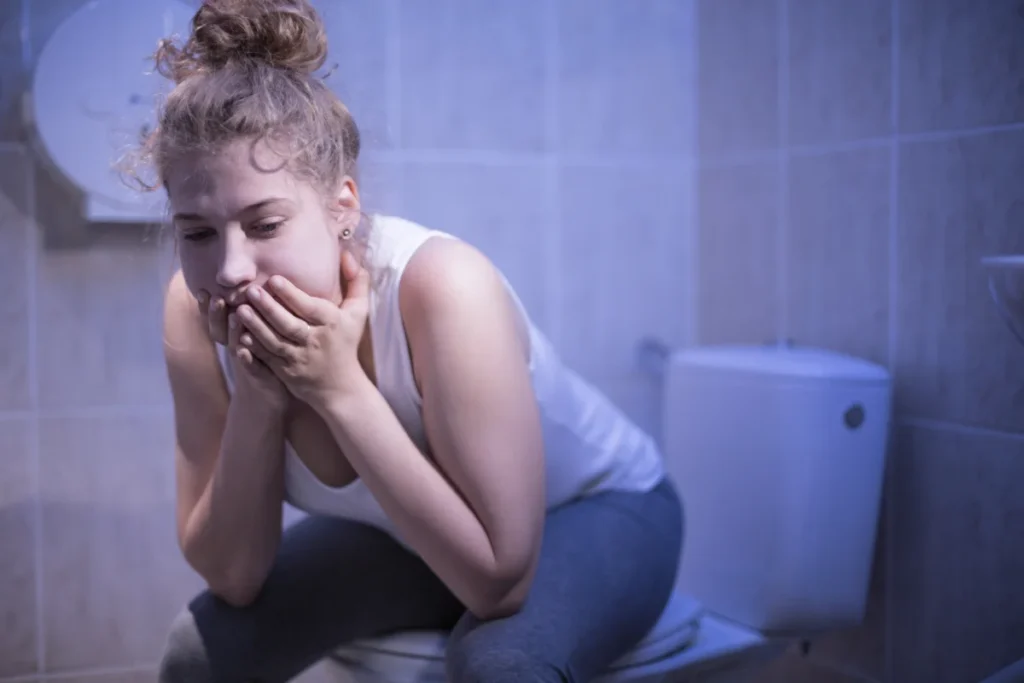 Mulher sentada no vaso do banheiro após provocar vômito devido à bulimia nervosa. 