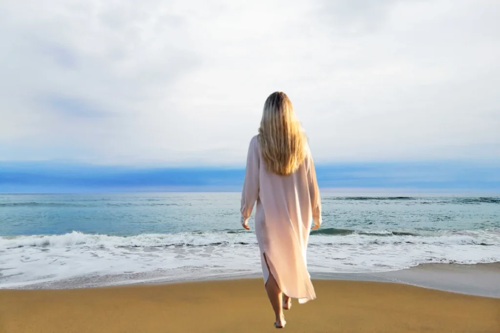 Mulher caminhando lentamente em direção ao mar, vencendo o medo aos poucos. 